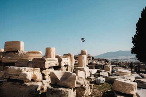 Free Scenic view of ancient ruins in Athens with the Greek flag flying high. Stock Photo