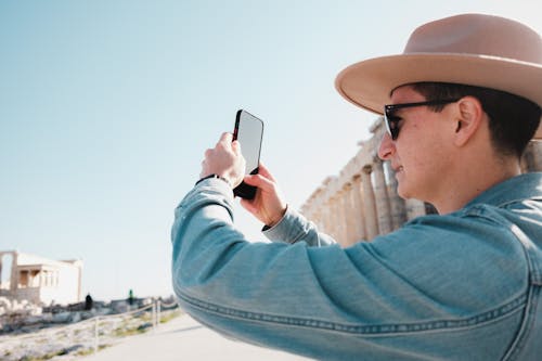 Man in Hat and Jean Jacket Taking Pictures with Smartphone