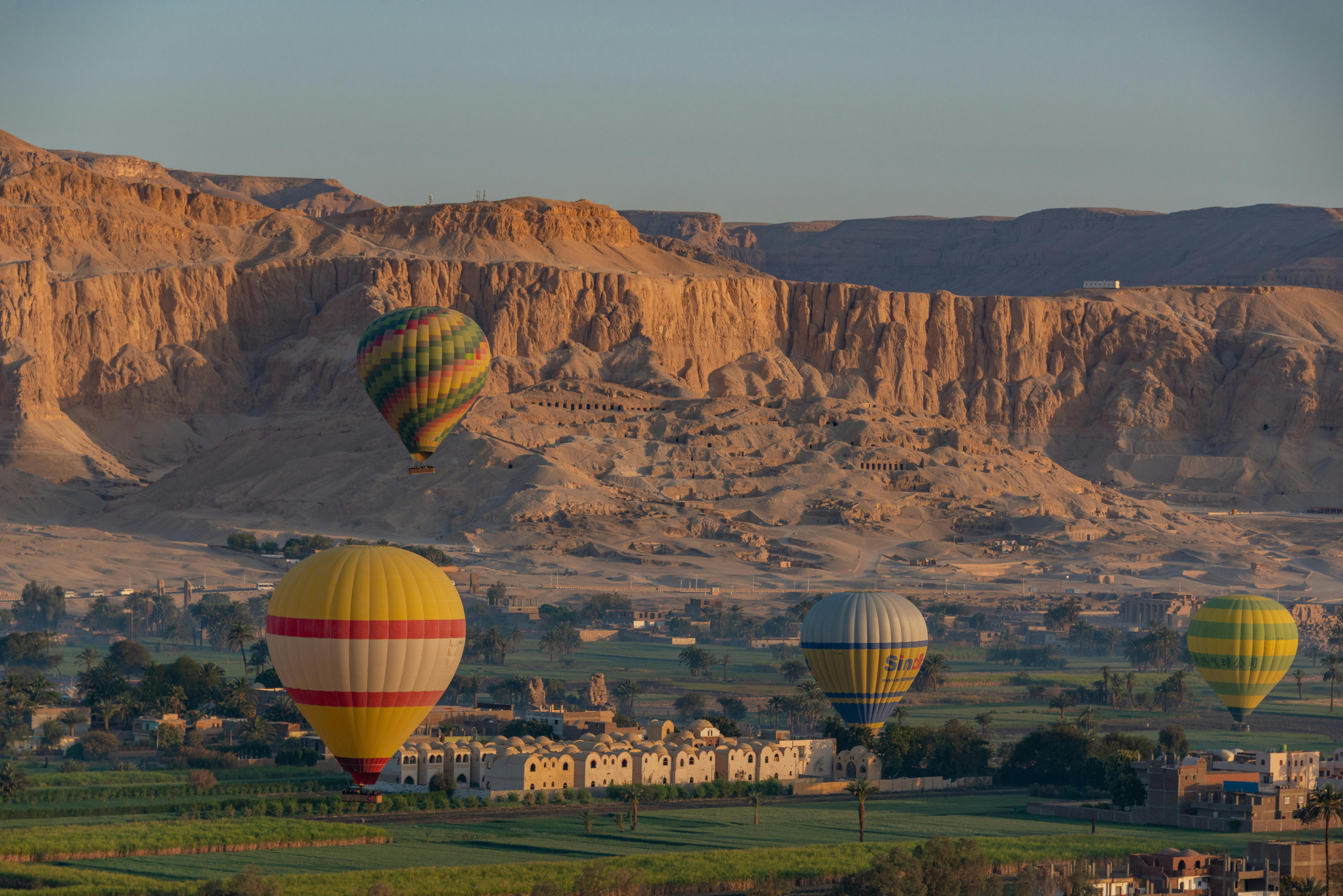 Serene view of hot air balloons flying over Luxor's landscape at sunrise with majestic rock formations.
