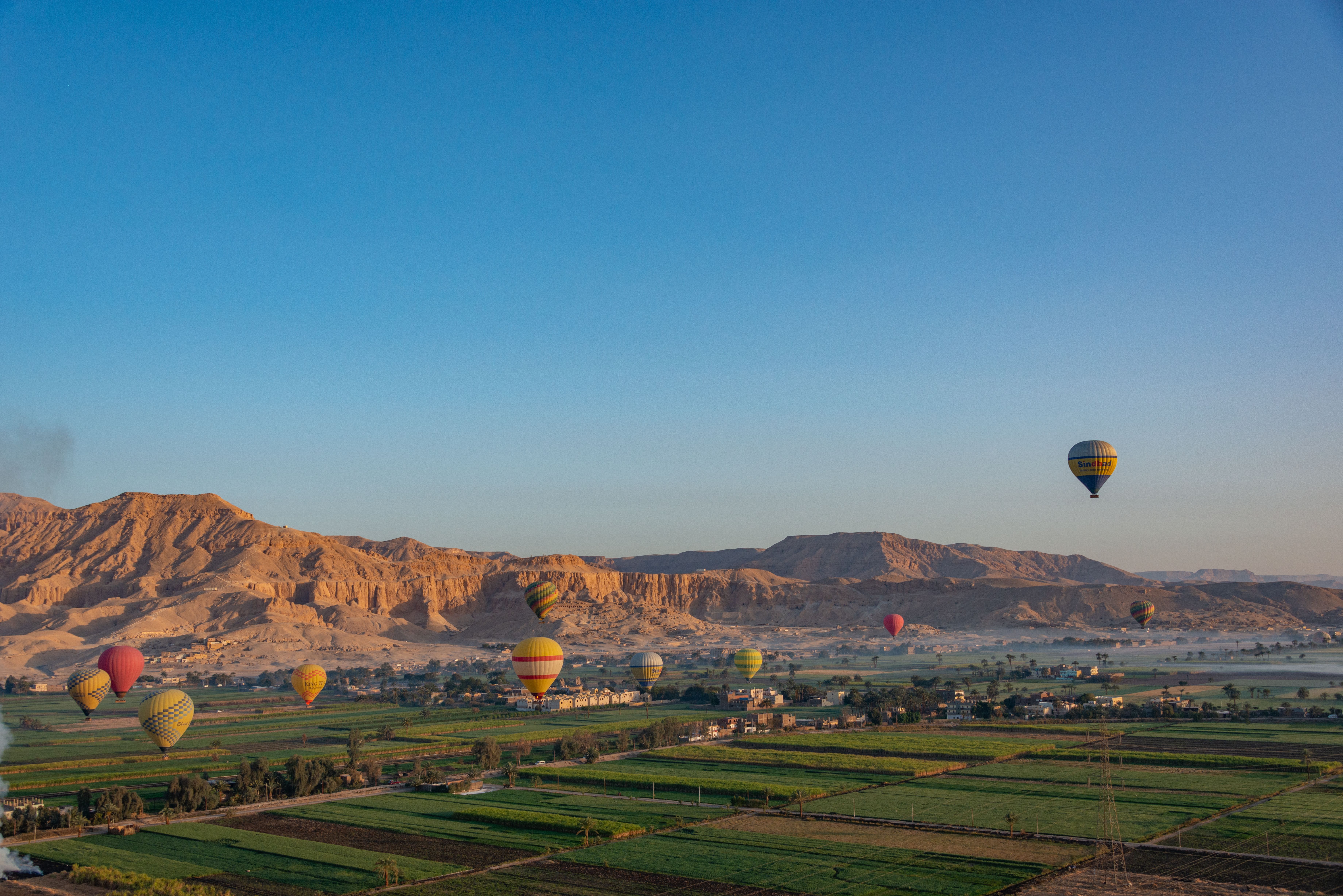 Vibrant hot air balloons soar over Luxor's fields, set against an Egyptian desert landscape.