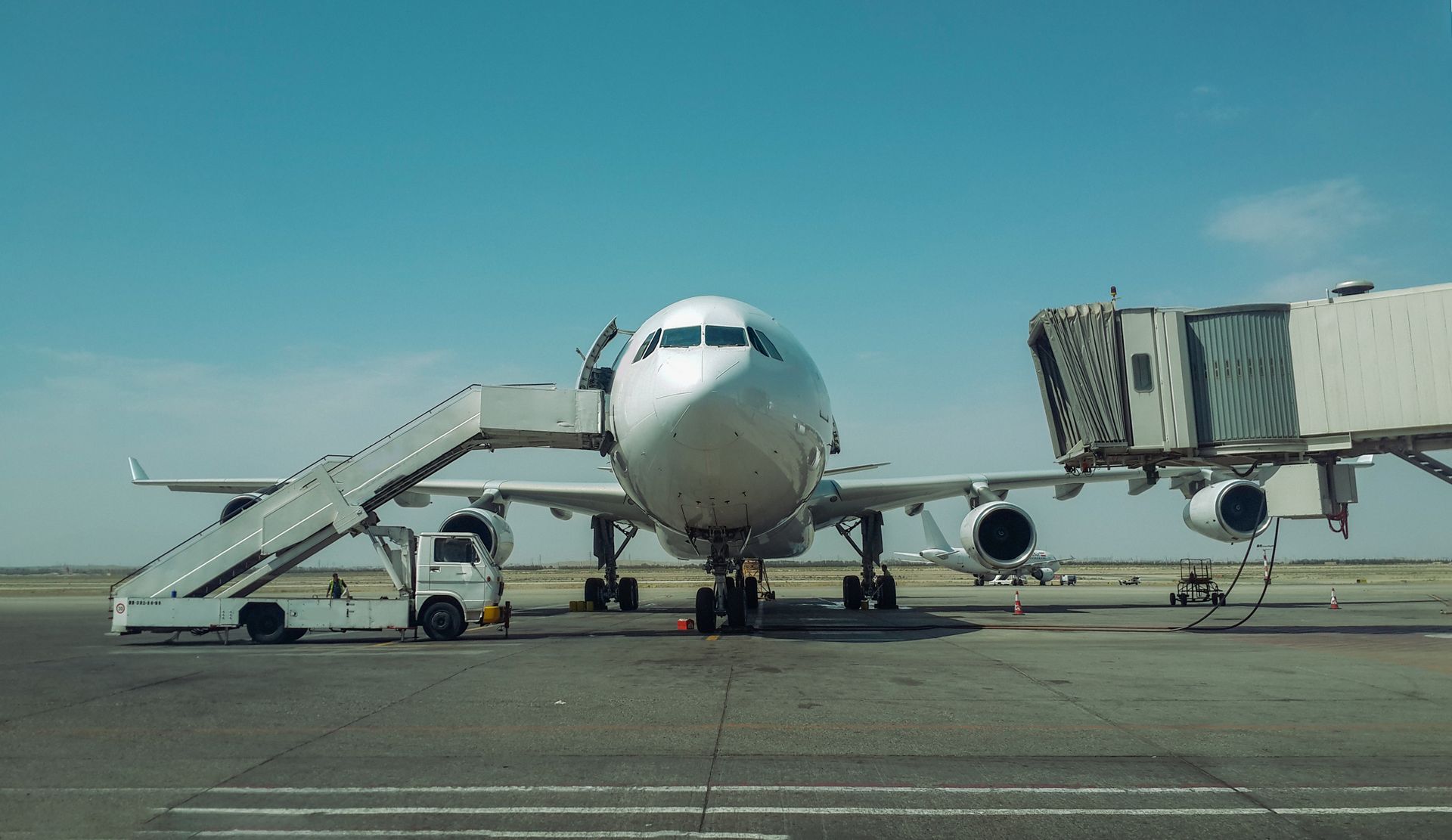 Large passenger plane stationed at Tehran airport with boarding stairs and bridge.