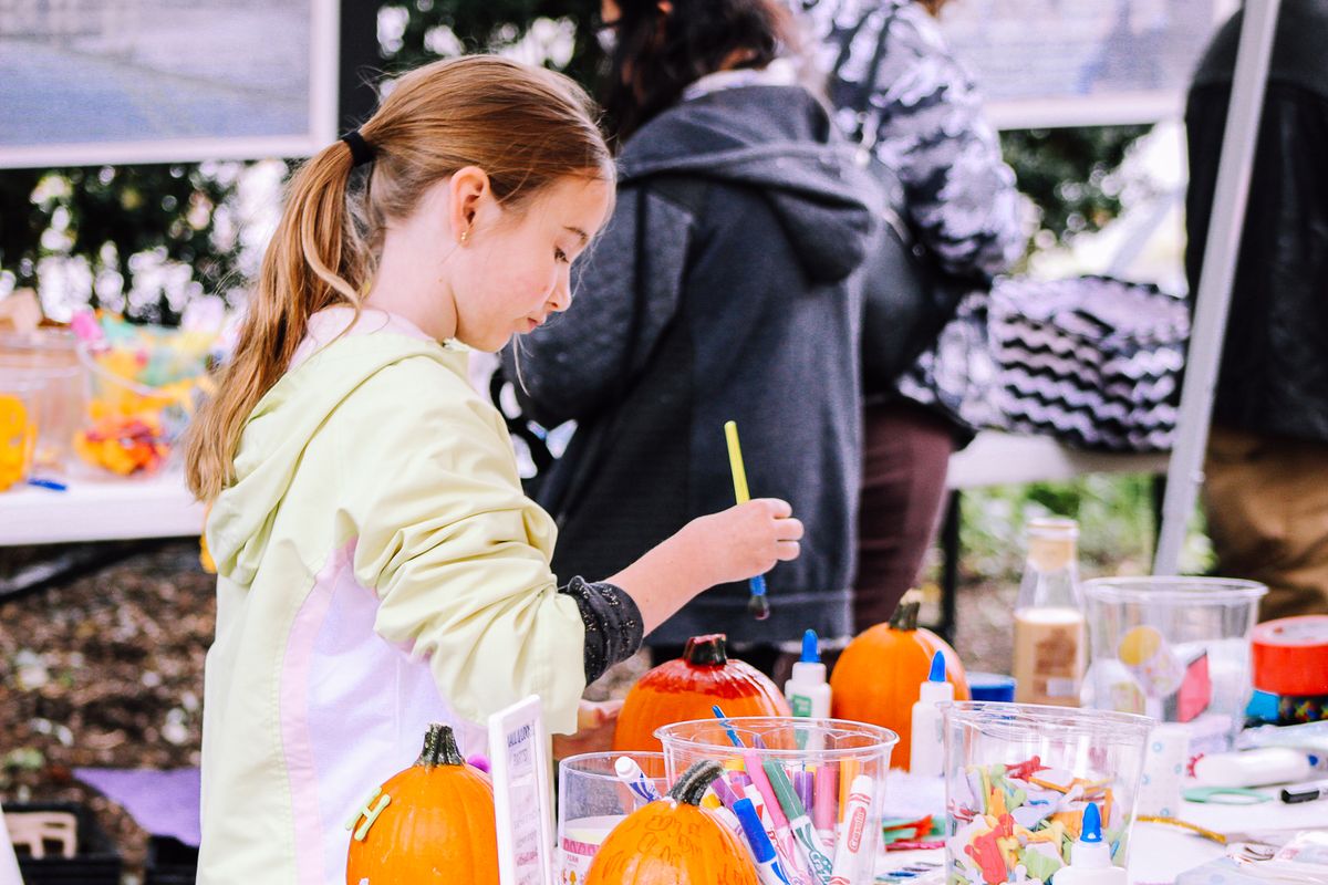 Child painting pumpkins at an outdoor crafting event surrounded by art supplies