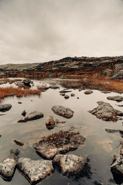 Free Tranquil rocky terrain with reflective water under overcast skies. Stock Photo