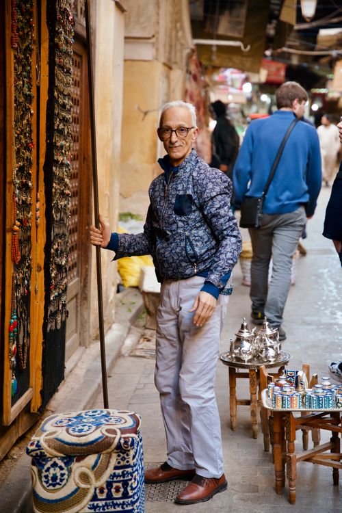 Free A cheerful vendor stands by his market stall in a bustling alleyway, offering souvenirs to passersby. Stock Photo