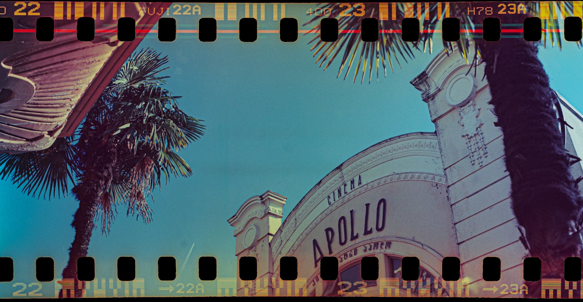 Film frame photo of Apollo cinema with palm trees, captured on a clear day in Batumi, Georgia.