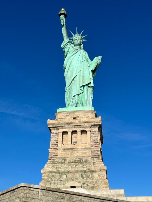 Free The Statue of Liberty stands majestically on Liberty Island with a vibrant blue sky backdrop. Stock Photo