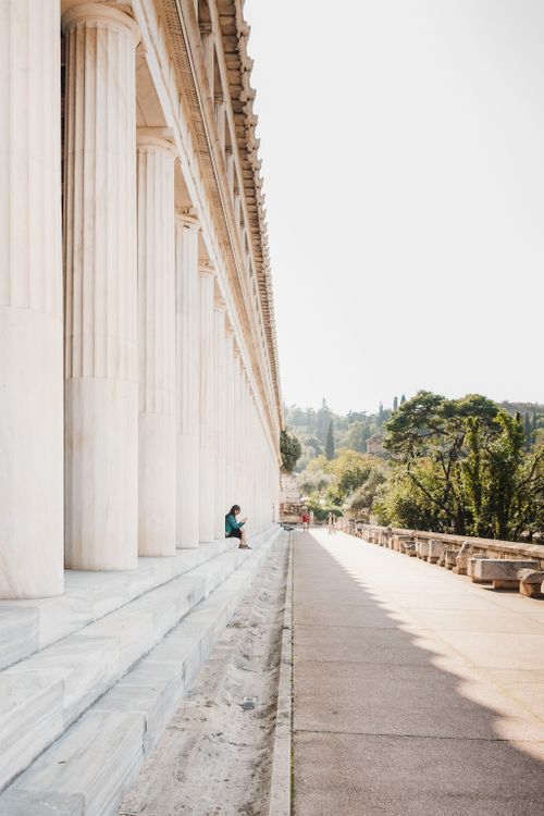 Free Vertical shot of historic columns with a solitary figure sitting, captured in a tranquil outdoor setting. Stock Photo