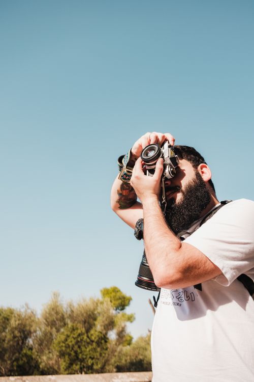 Free Photographer with an analog camera taking a picture under a clear blue sky. Stock Photo