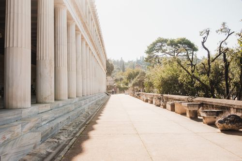 Free Beautiful sunlit view of the Stoa of Attalos with its classic columns and surrounding greenery in Athens. Stock Photo