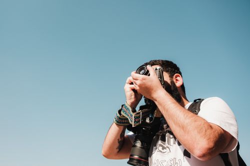 Free A man takes photos with a camera against a clear blue sky. Daytime outdoor photography scene. Stock Photo