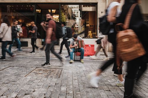 Free A street musician plays the accordion amidst bustling pedestrians on a busy sidewalk. Stock Photo
