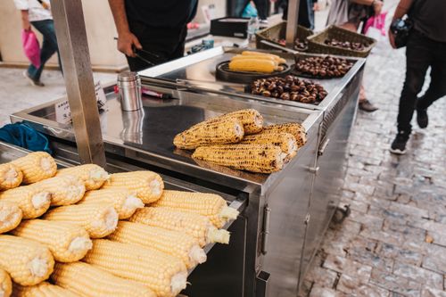 Free A bustling street food stand offering roasted corn and chestnuts in an urban market setting. Stock Photo