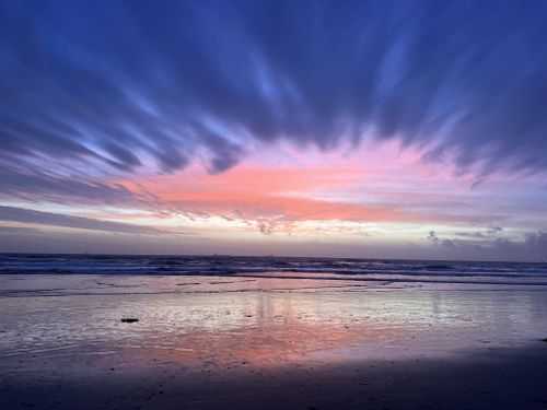 Free Sunset at Huntington Beach with vibrant sky reflections on the ocean shore. Stock Photo