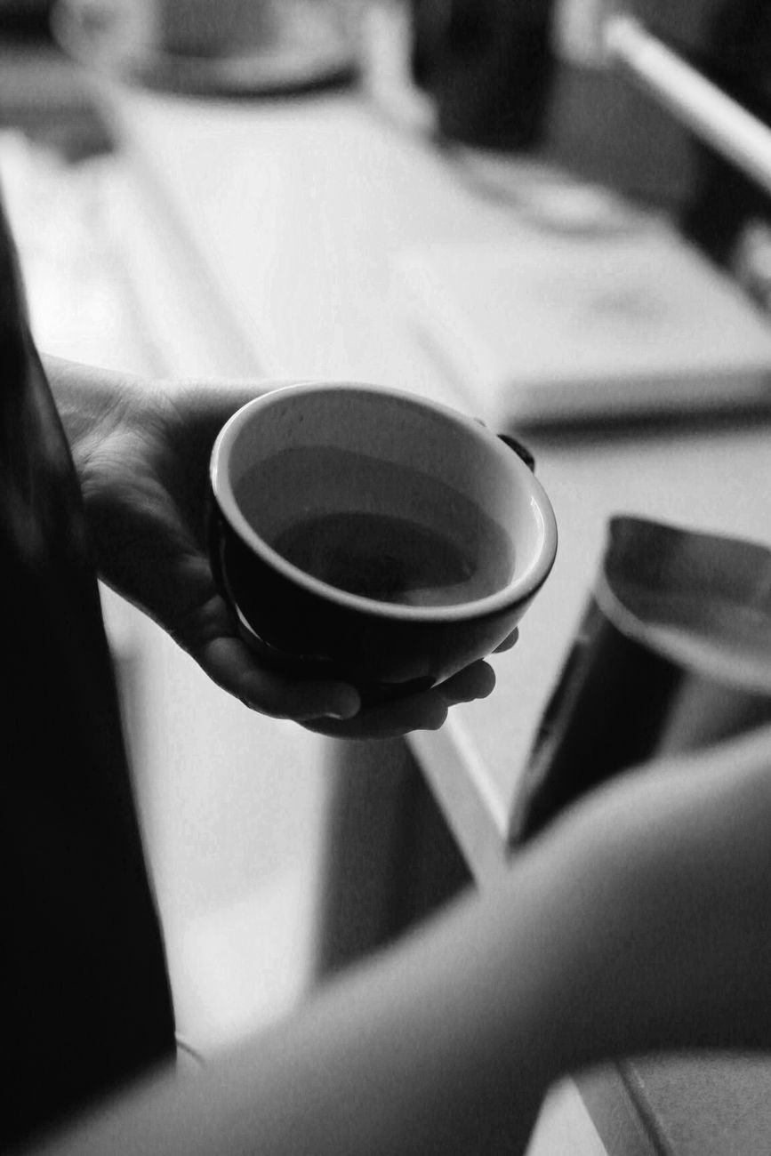 A black and white close-up of a person holding a coffee cup, preparing a drink.. black, white, close