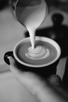 Elegant black and white capture of coffee pour creating latte art in a cafe.
