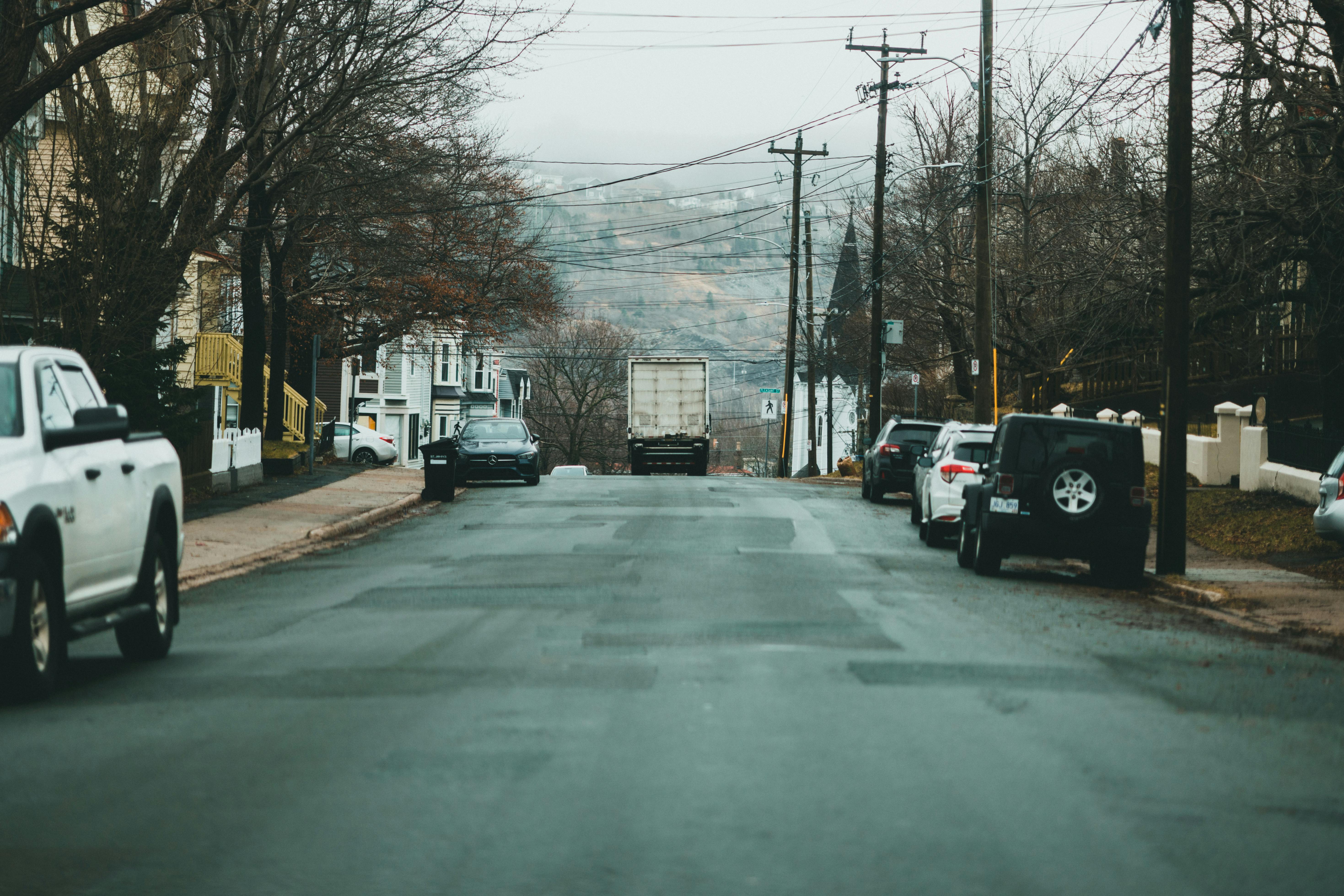 Urban street lined with parked cars in a quiet suburban neighborhood during a cloudy day.