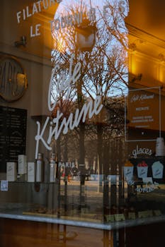 Reflection of trees in a Parisian café window during winter, capturing the essence of urban life.