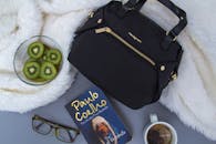 从上面看，灰色床上铺着白色毛皮毯子，上面放着一碗新鲜的猕猴桃片、一杯茶、一个经典的袋子和一副带眼镜的书