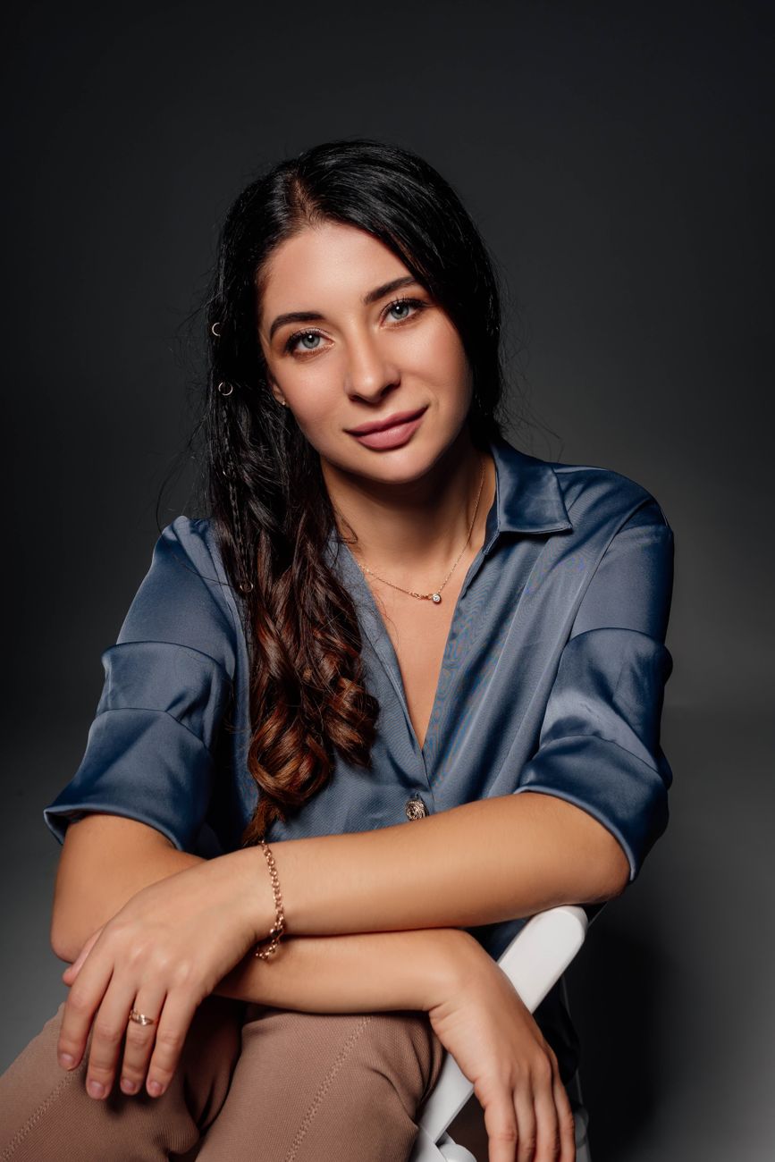 Portrait of a young brunette woman sitting on a chair with a confident smile in a studio setting.