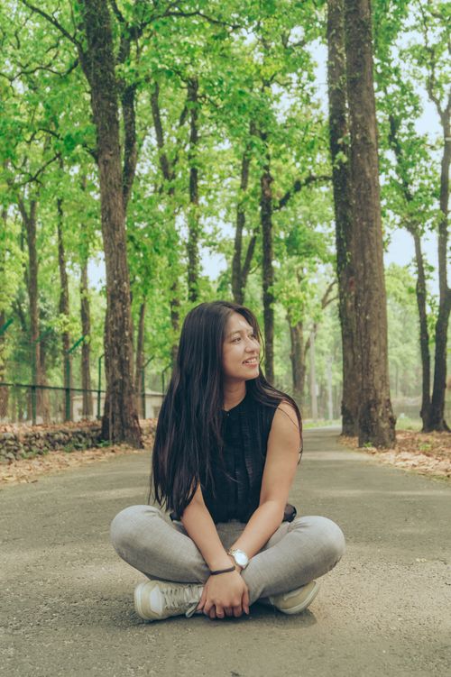 Free Smiling young woman with long hair sits cross-legged on a forest path in spring. Stock Photo