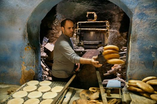 A baker uses a wooden paddle to remove freshly baked bread from a traditional oven.