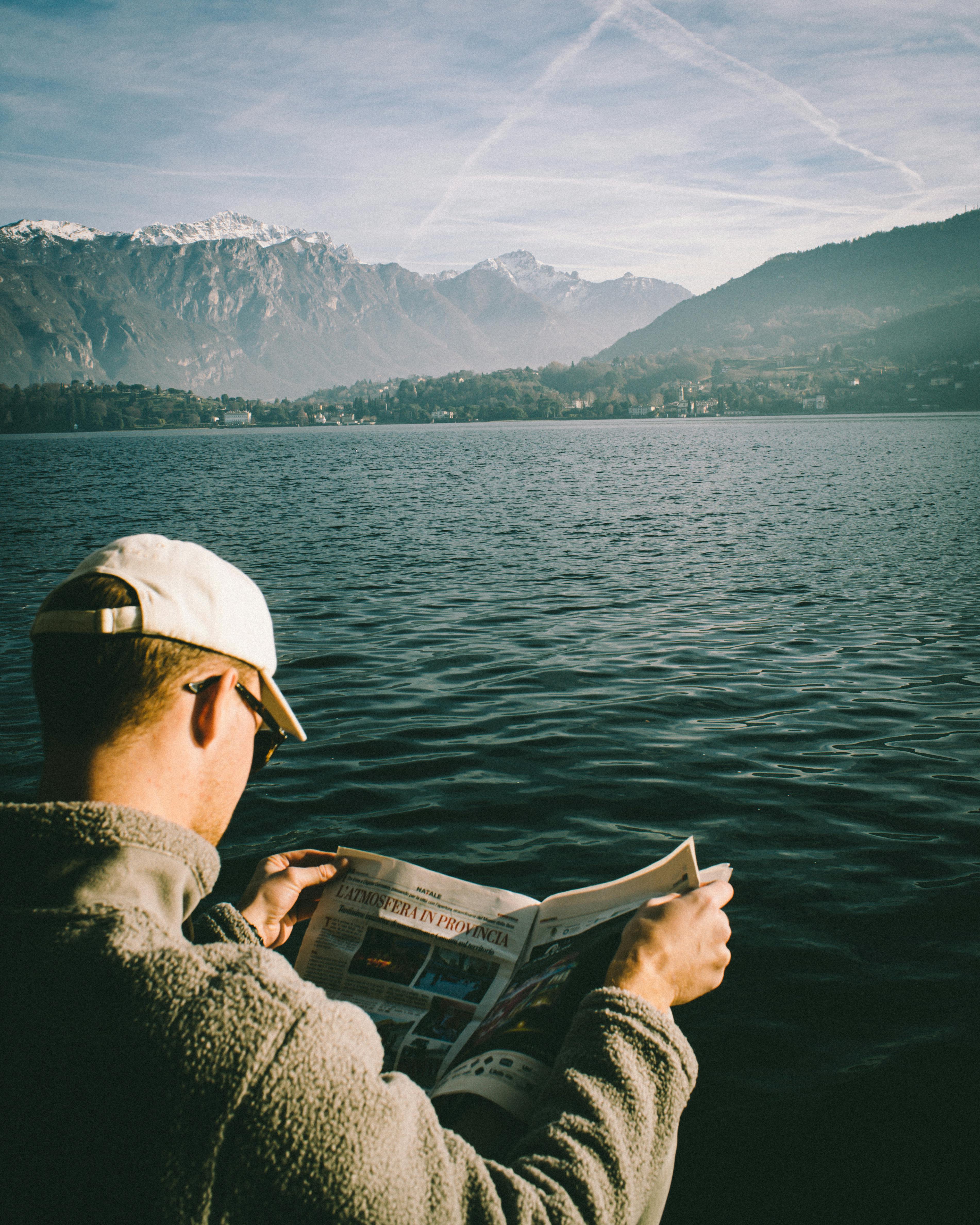 Serene image of a man reading by Lake Como with mountain backdrop.