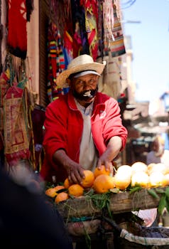 A vibrant street market scene featuring a man selling fresh fruit, surrounded by colorful fabrics.