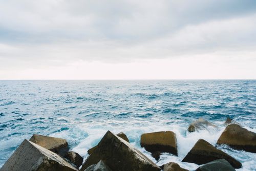 Free Rocky coast with waves splashing under an overcast sky, creating a dramatic seascape. Stock Photo