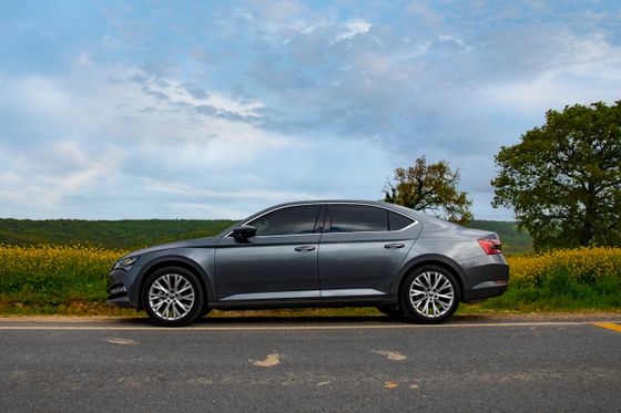Grey saloon in side profile on a country road beside a field of yellow rape. Photo by Emrah AYVALI on Pexels