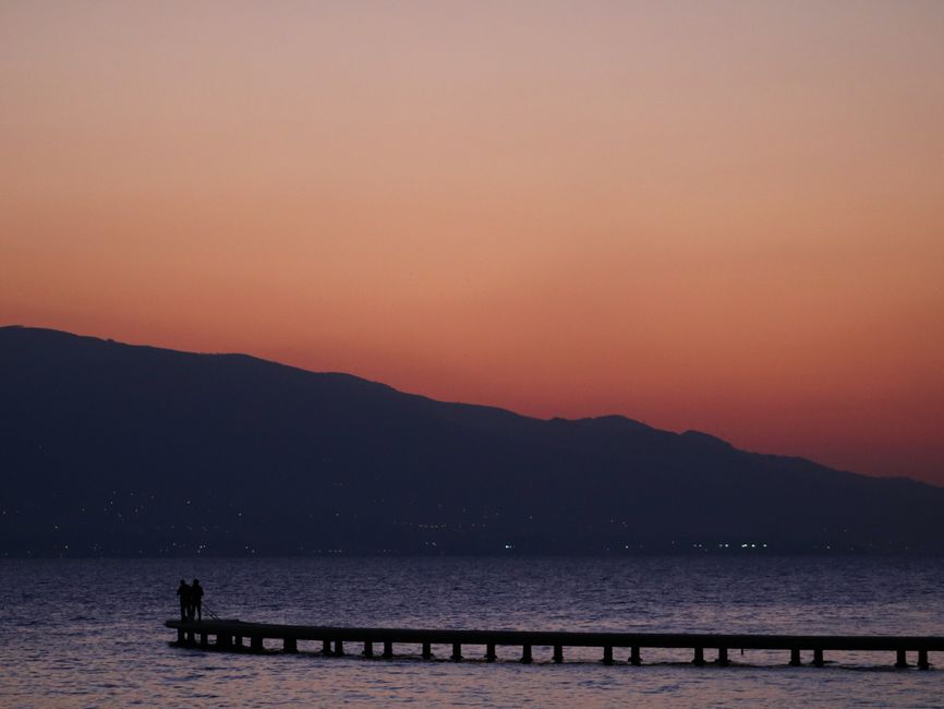 Serene sunset view from İzmit, capturing silhouettes on a pier against a tranquil orange sky.