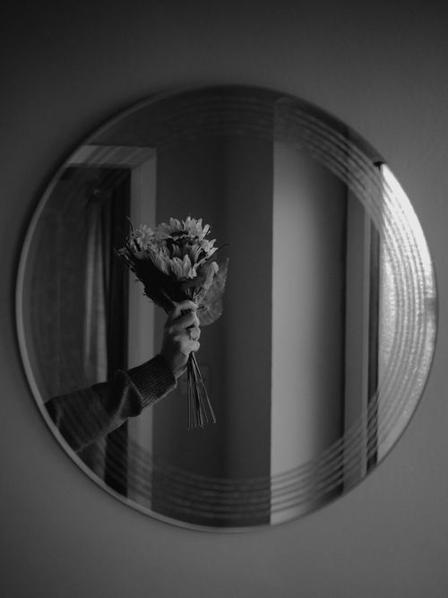 Free Black and white image of a hand holding a bouquet reflected in a round mirror. Stock Photo