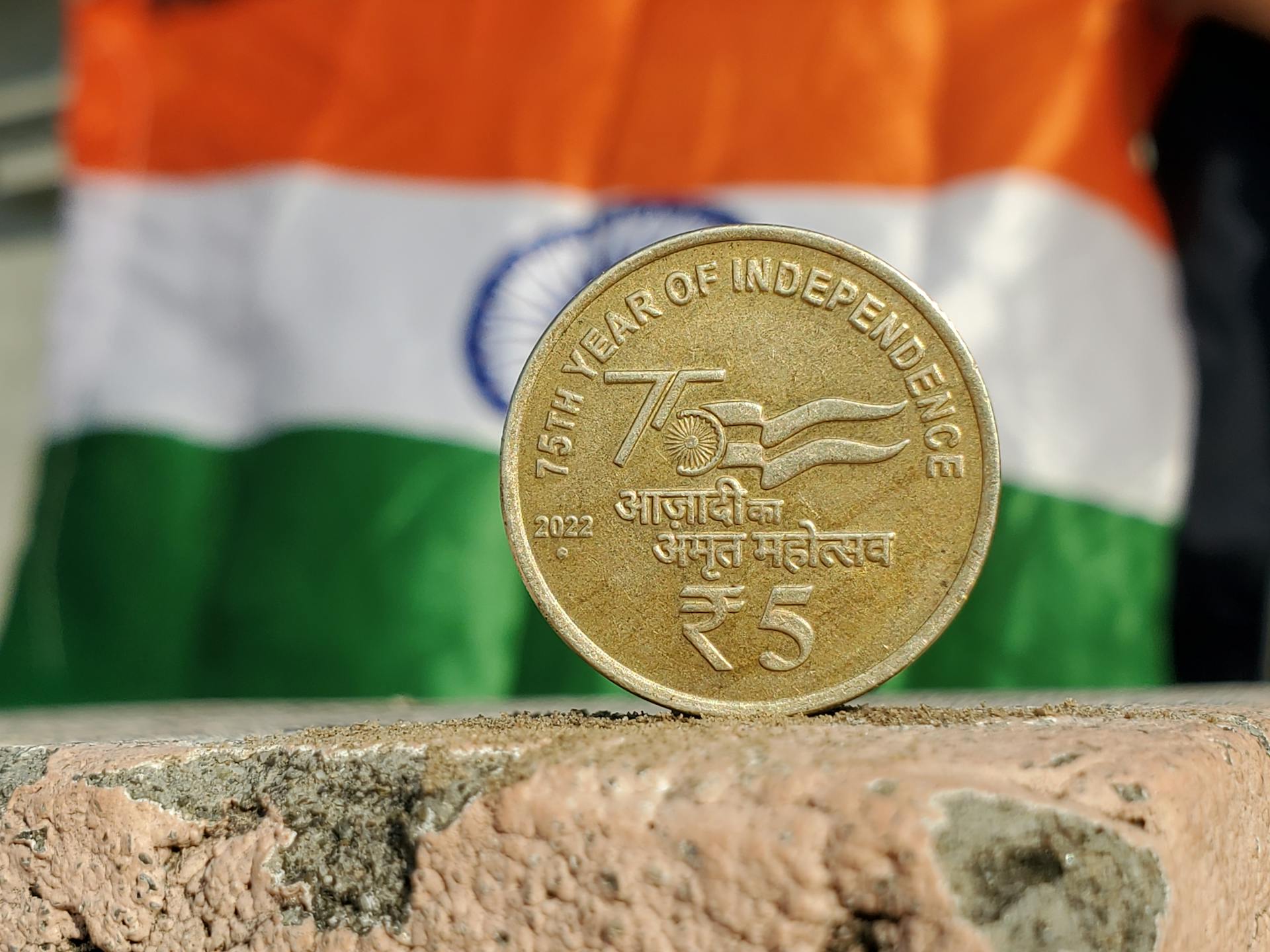 Close-up of a 5 Rupee coin commemorating India's 75th year of independence, set against the Indian flag.