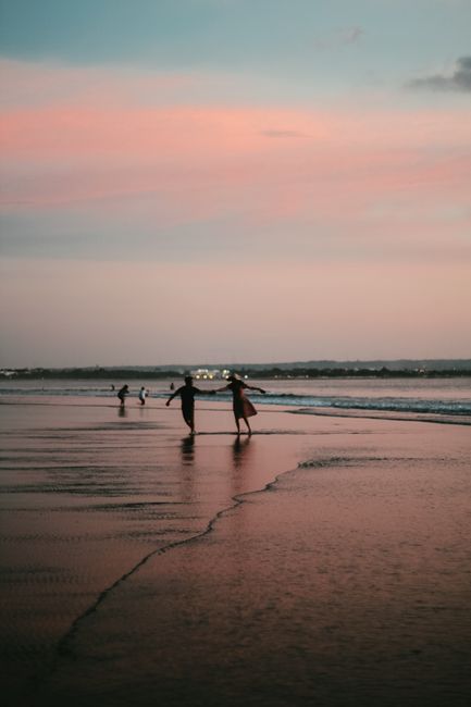 Couple holding hands and running on a tranquil beach at sunset.