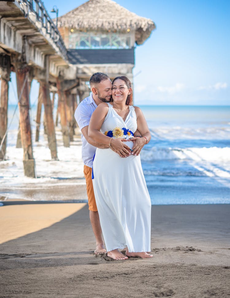 A Man Hugging A Pregnant Woman At The Beach