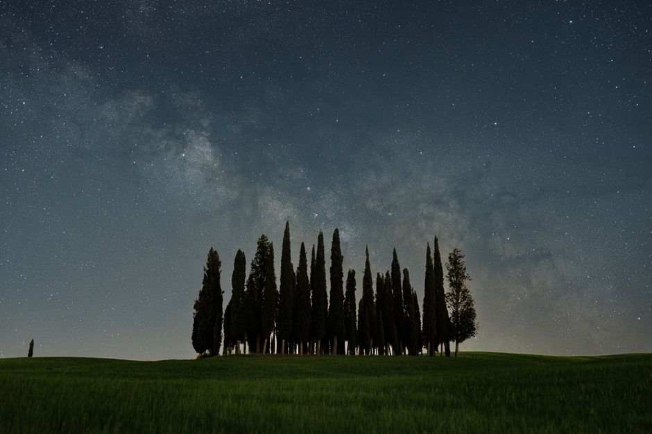 Cypress trees under a vibrant Milky Way in San Gimignano, Tuscany. A serene night landscape.