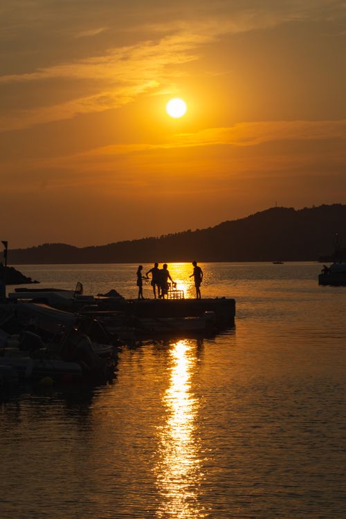 Free A beautiful sunset silhouette of people on a dock in Nea Skioni, Greece, capturing a serene coastal evening. Stock Photo