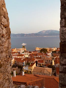 A breathtaking view of Nafpaktos, Greece, showcasing red-roofed buildings and the tranquil sea through a stone frame.