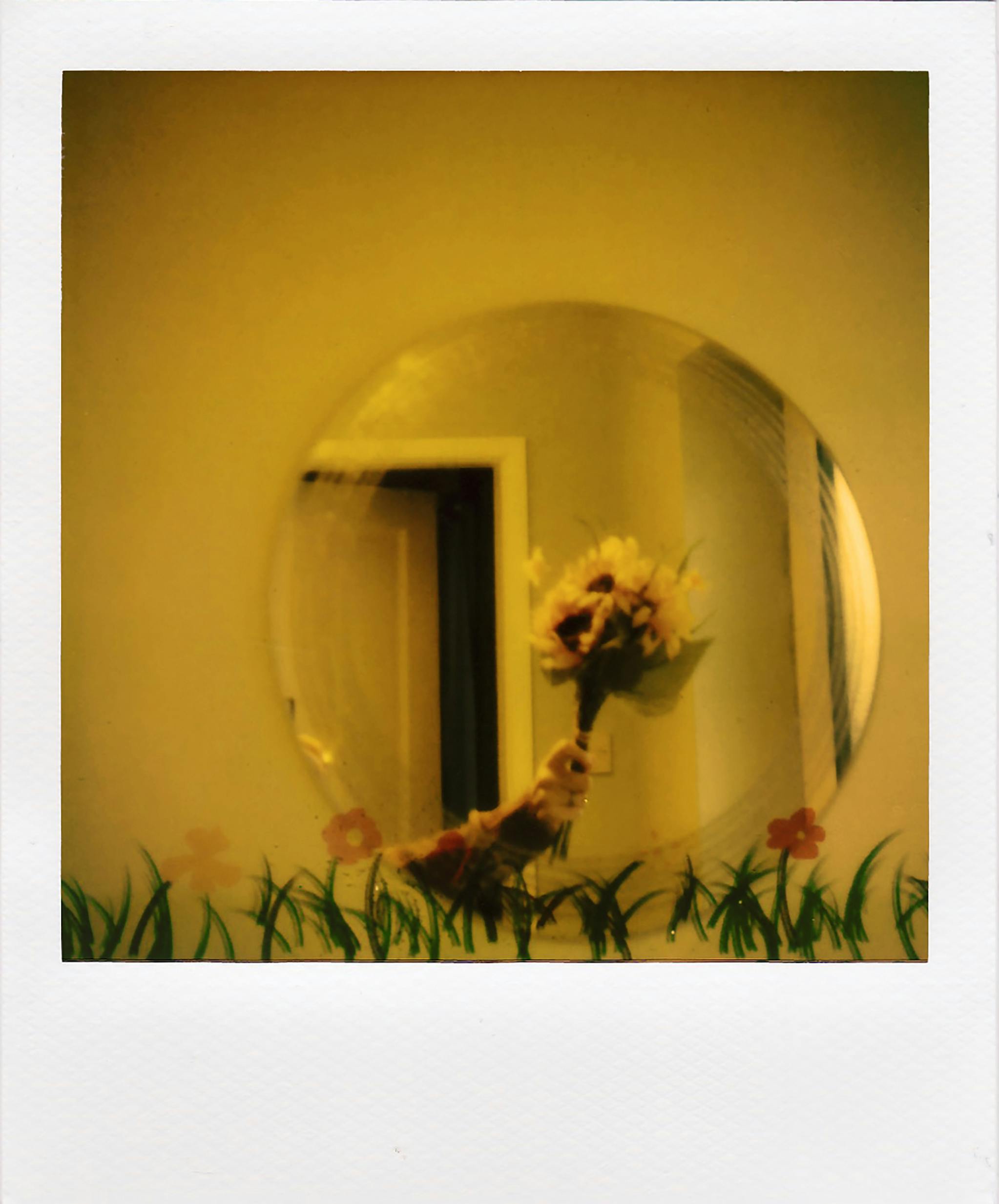 A hand holding a bouquet is creatively reflected in a circular mirror, surrounded by painted flowers on a yellow background.