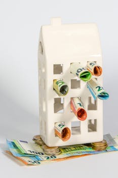 Ceramic house piggy bank stuffed with rolled euro notes and stacked coins, symbolizing real estate investment and savings.
