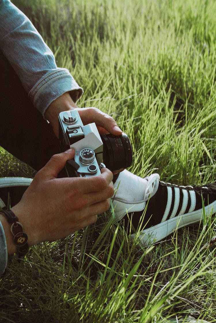 Photo Of A Man Sitting On The Grass And Holding In Hands A Camera