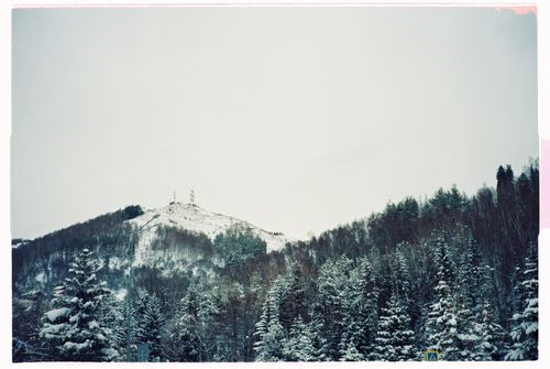 Free A peaceful winter landscape featuring a snowcapped mountain and dense forest under an overcast sky. Stock Photo