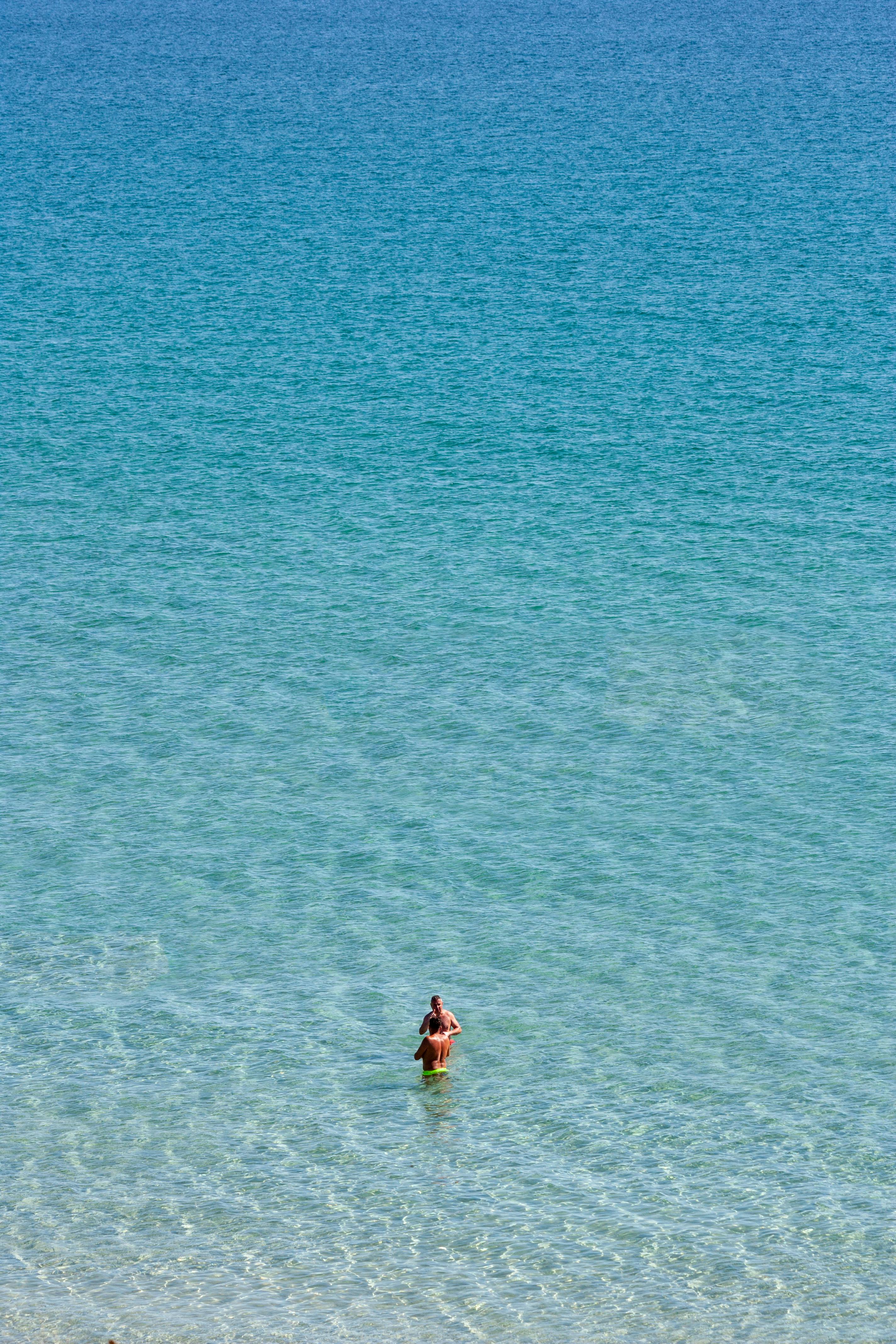 An individual standing alone in calm, clear ocean waters, viewed from above. Perfect for themes of solitude and nature.