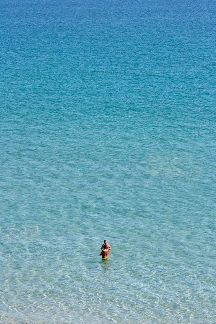 An individual standing alone in calm, clear ocean waters, viewed from above. Perfect for themes of solitude and nature.