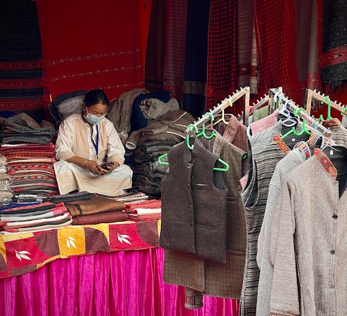 Woman Sitting inside Market Stall Selling Coats