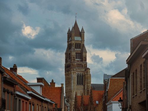 Free A towering view of St. Salvator's Cathedral in Bruges amidst an urban environment with a dramatic cloudy sky. Stock Photo