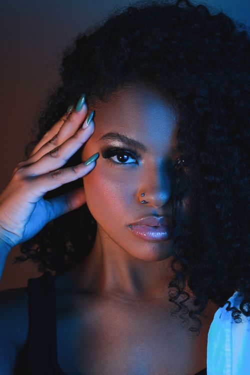 Free Striking portrait of a young woman with blue lighting and curly hair, conveying confidence and style. Stock Photo