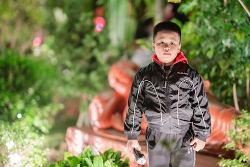 Boy in Black Jacket Standing Near Green Plants