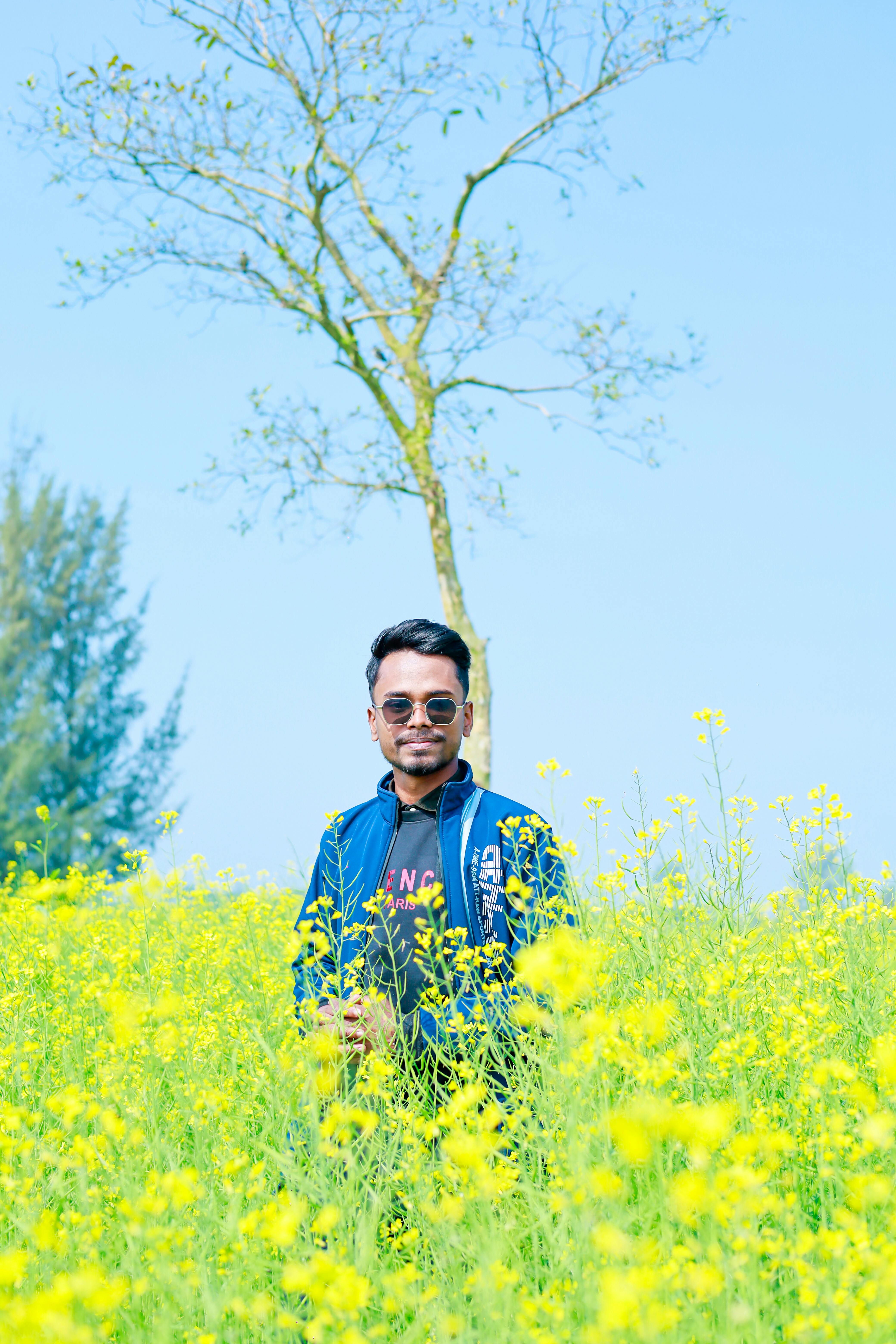 A man stands amid blooming mustard fields under a clear blue sky, capturing the essence of rural beauty.