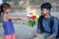 A young girl offers a colorful bouquet to a smiling man sitting outside, capturing a heartfelt moment.