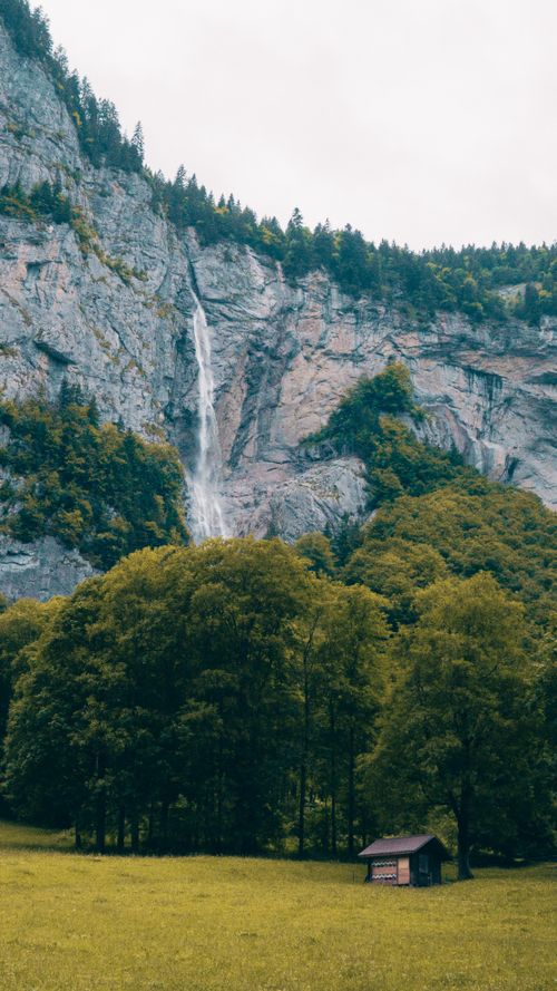 Free A serene landscape featuring a stunning waterfall cascading down a rocky mountain surrounded by lush trees. Stock Photo